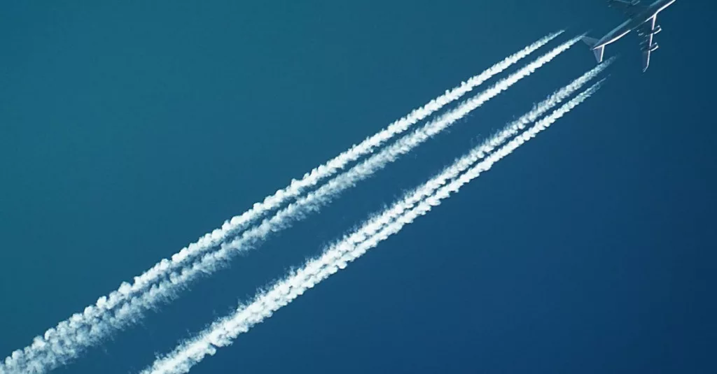 Aerial view of an airplane in flight, leaving vapor trails against a clear blue sky.